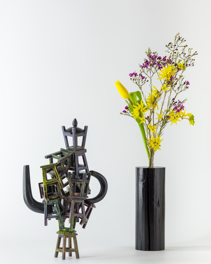 Black wooden vase with flower arrangement beside wooden sculpture
