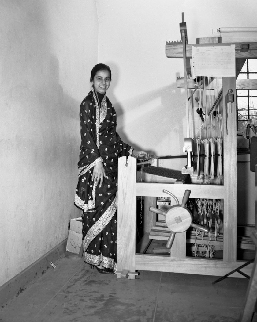 Black and white photo of textile artist in Indian dress posing beside large wooden loom