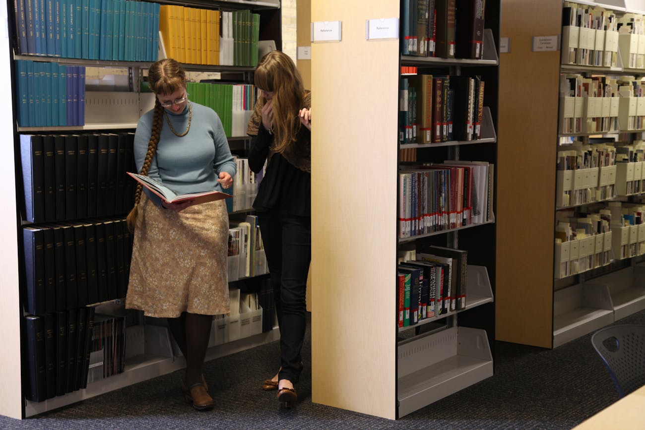 two researchers looking at a book together in library stacks