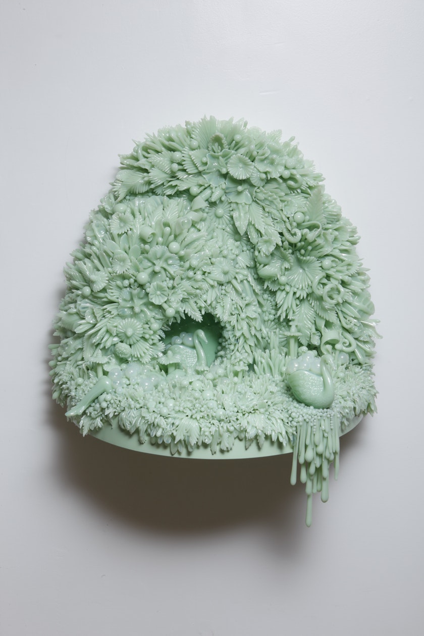 egg shaped wall sculpture made from countless mint green glass leaves and pedals with two swans moving through a bubbly tunnel mounted on a gray wall