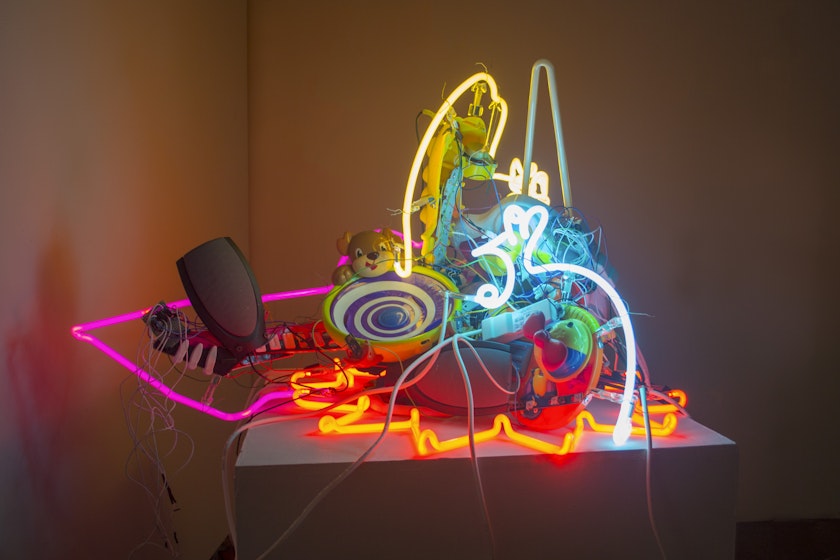 sculpture with chaotic arrangement of glowing neon glass shapes and various electronic equipment and toys