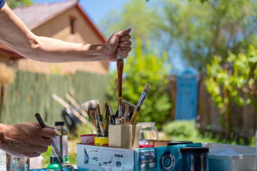 artist selecting brushes from an assortment in jars and cans in an outdoor studio on a sunny day