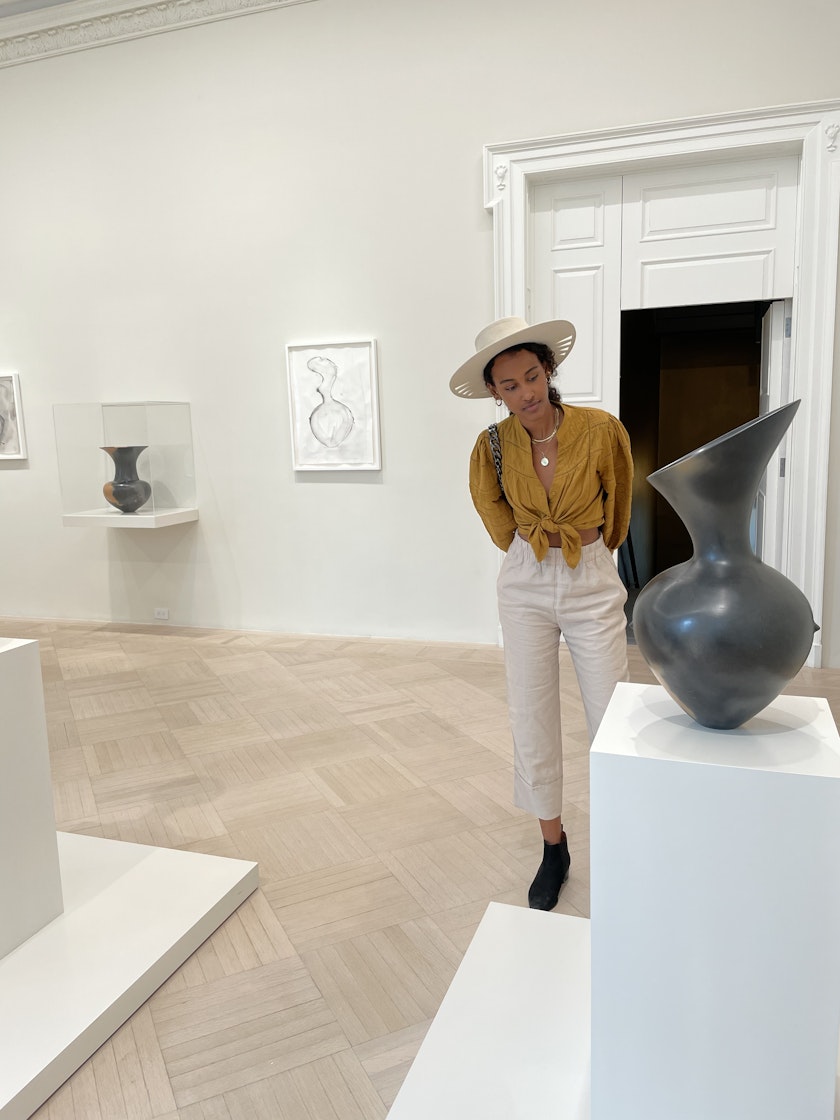 A woman studying a ceramic vessel on a white pedestal in an exhibtion gallery
