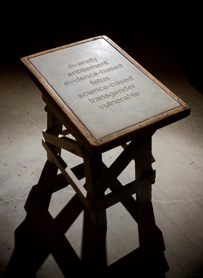 spot-lit wooden pedestal holding stone plaque with seven controversial words carved into it