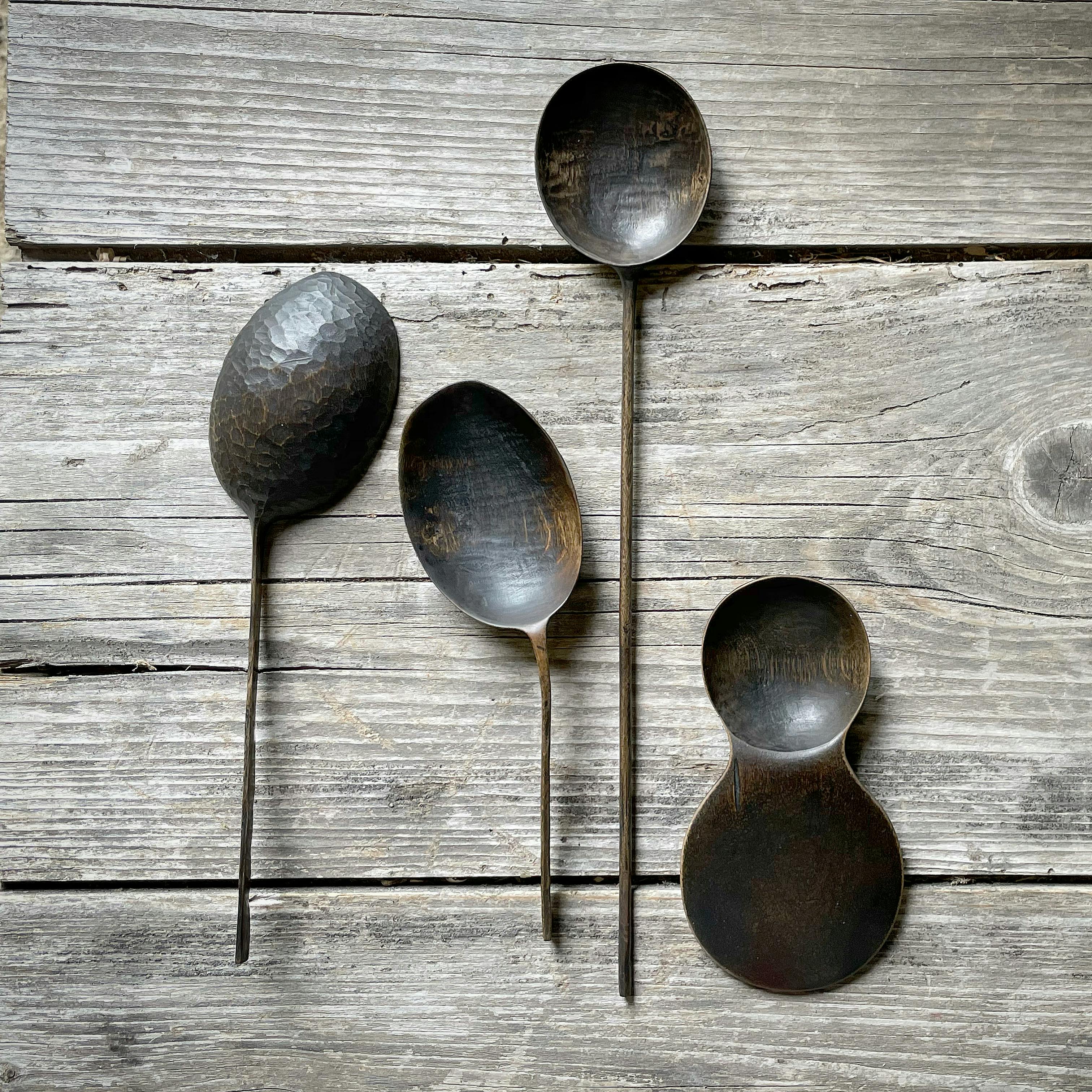 Four handmade wooden spoons of varied shapes pictured on wood planks
