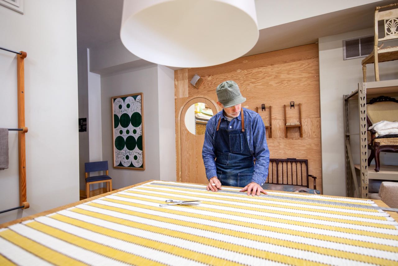 Upholstery artist measuring yellow striped fabric on a table in a studio