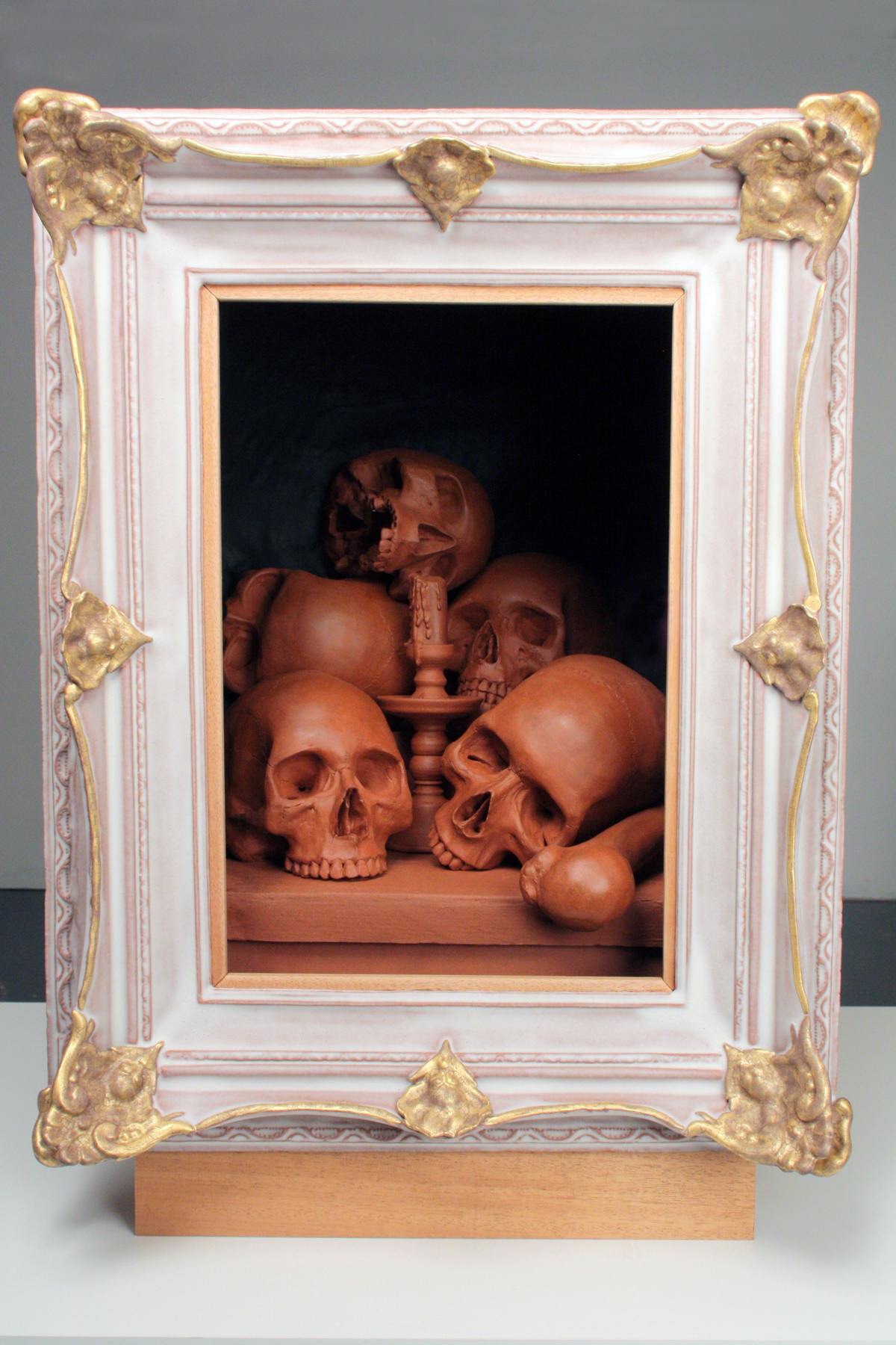 pink and gold picture frame housing a depiction of skulls and other bones in a clay hue