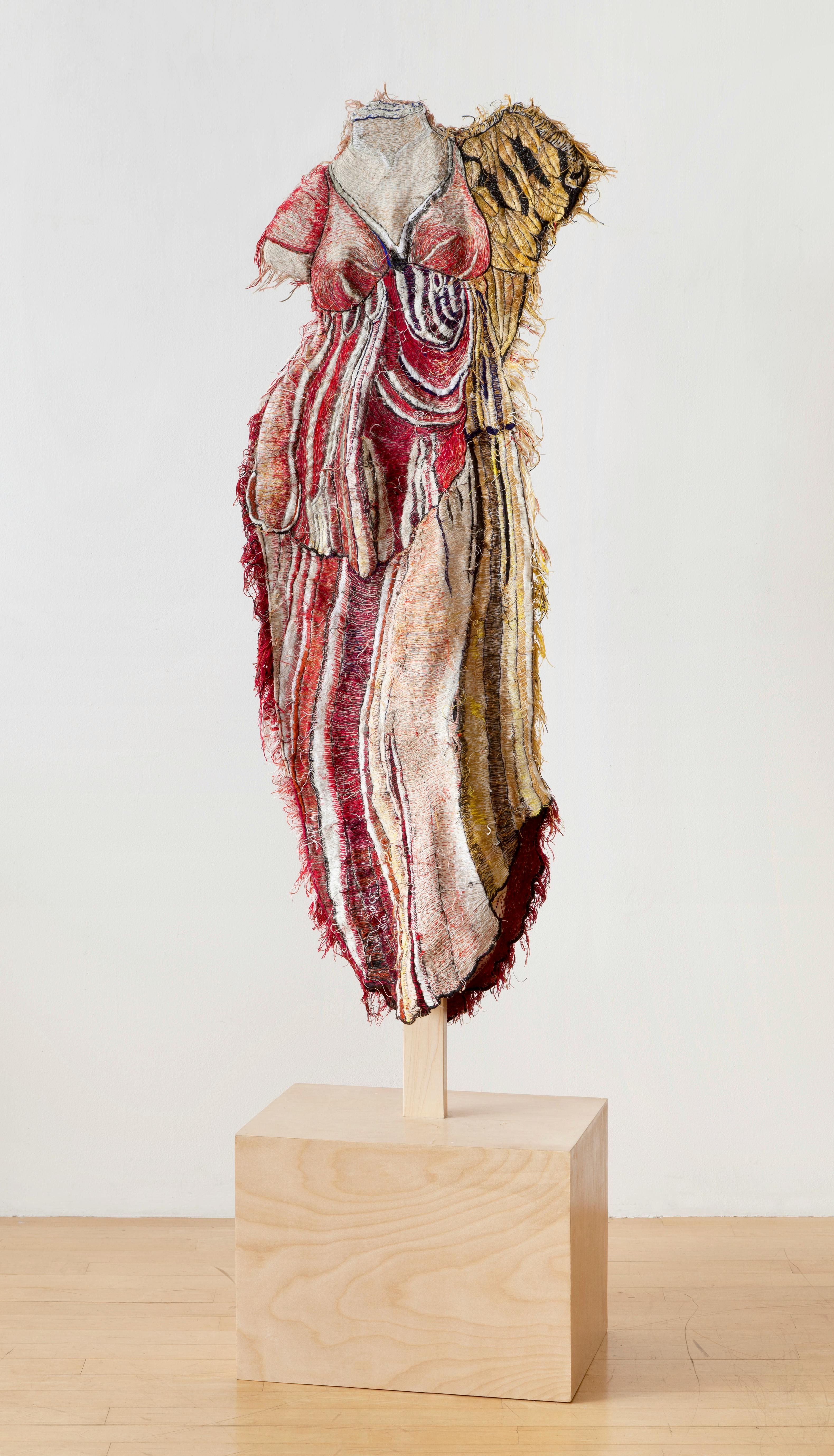 textile sculpture reminiscent of a Grecian dress displayed on a wood pedestal