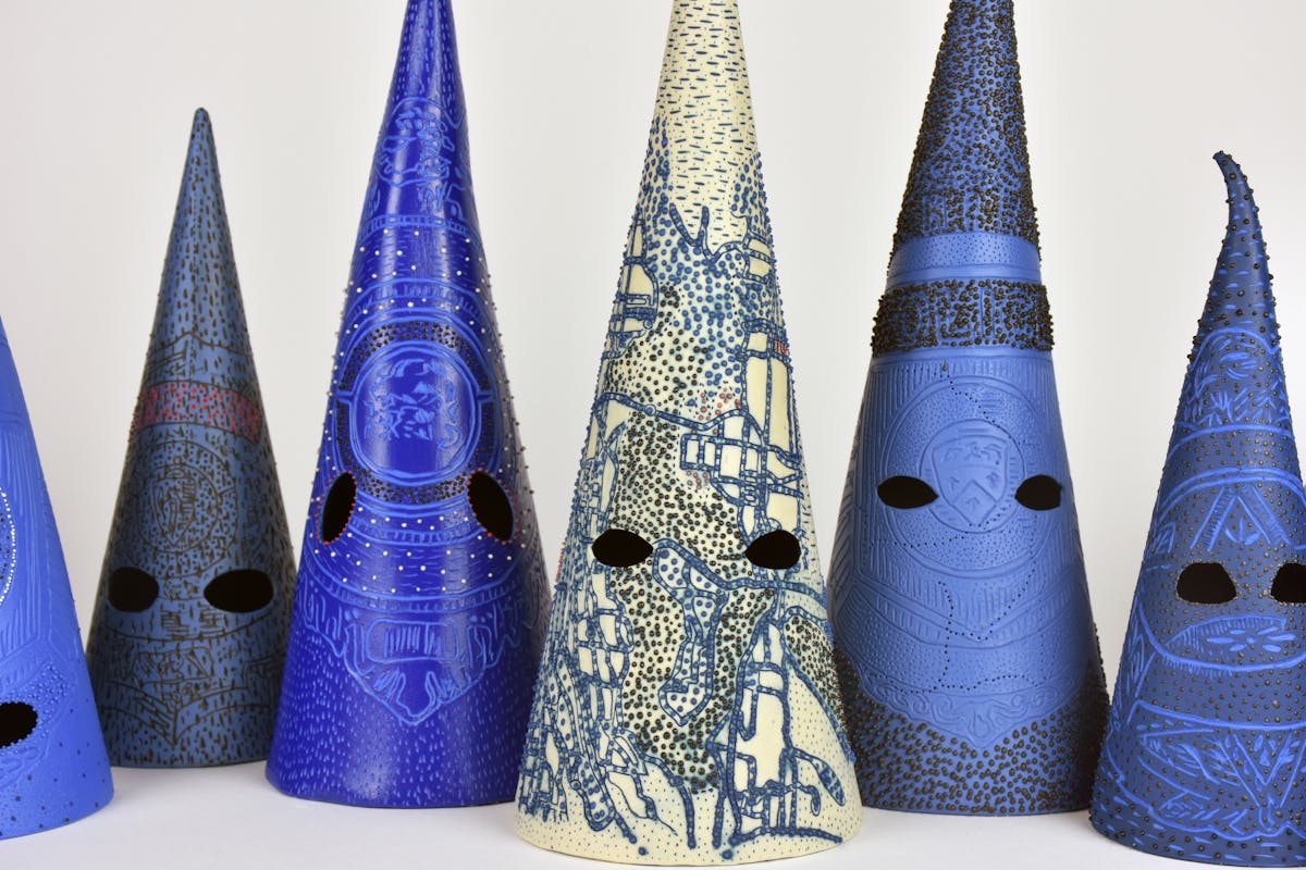 ceramic sculptures of conical face masks that are blue and etched with roads and other symbols
