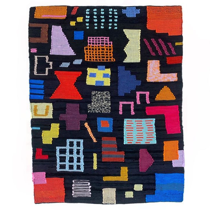 screenshot of an instagram post showing a handwoven rug with various colorful symbols and shapes on a black background