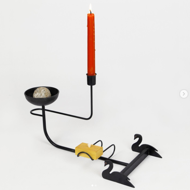 screenshot of an instagram post showing a minimalist whimsical black metal candelholder with red candle