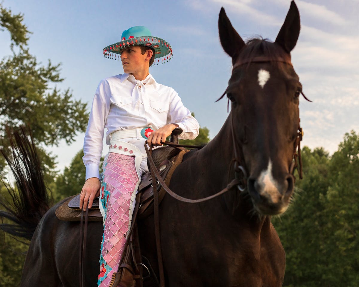 portrait of shae bishop on horseback wearing ornate teal blue cowboy hat white shirt and ornate chaps made from pink and blue ceramic tiles