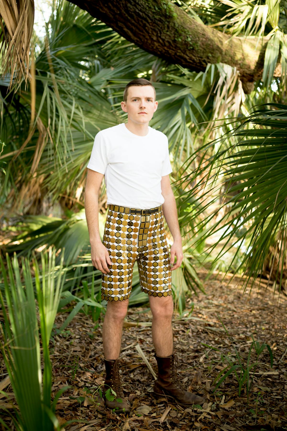 shae bishop standing in forest wearing white shirt and shorts made from brown ceramic tiles 