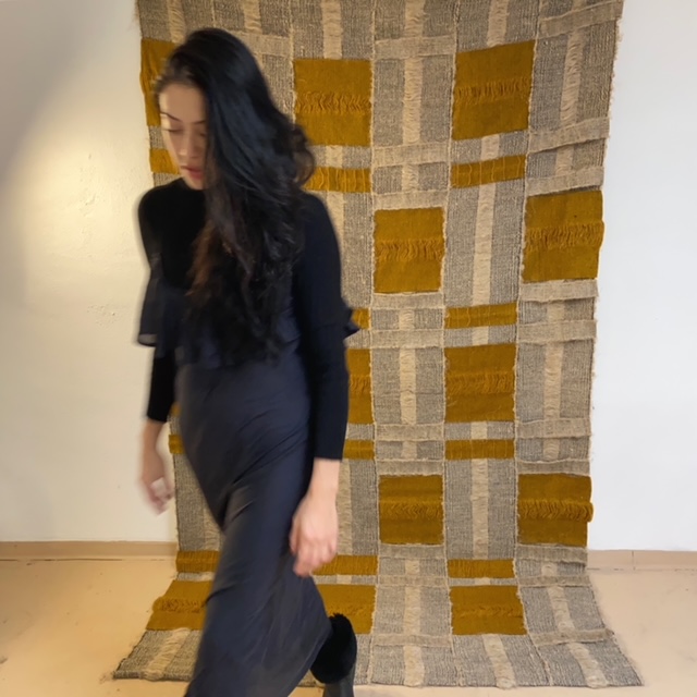 textile artist rhiannon griego in motion walking away from brown and tan handwoven textile artwork