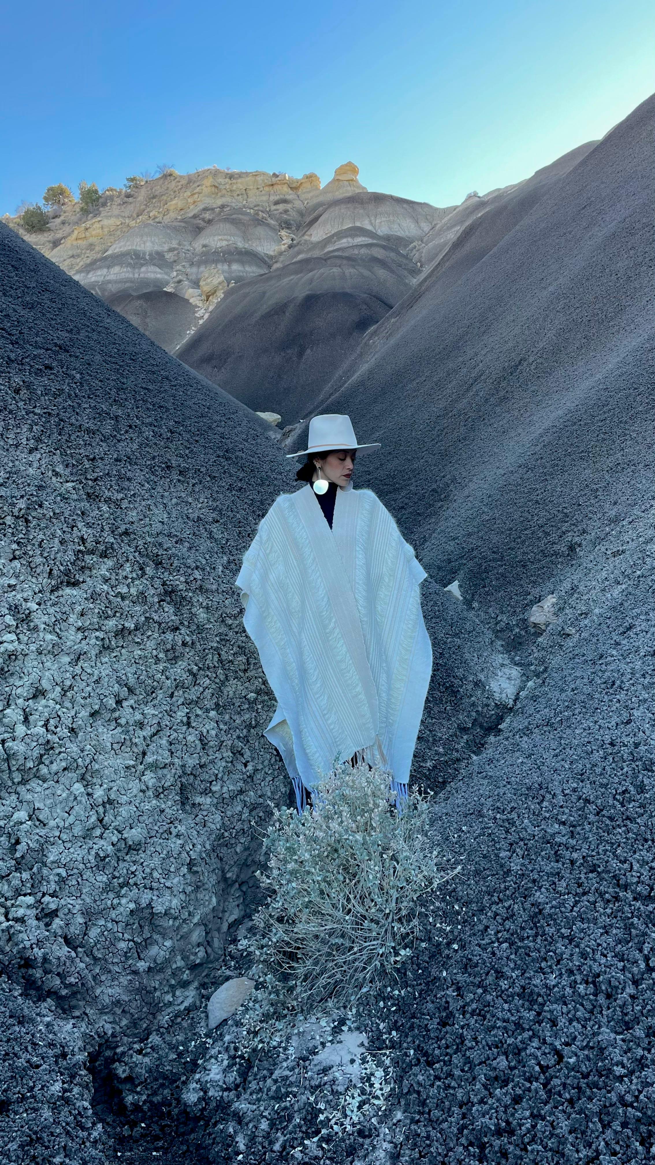 textile artist rhiannon griego in fashionable white poncho and hat posing in desert canyon at dusk