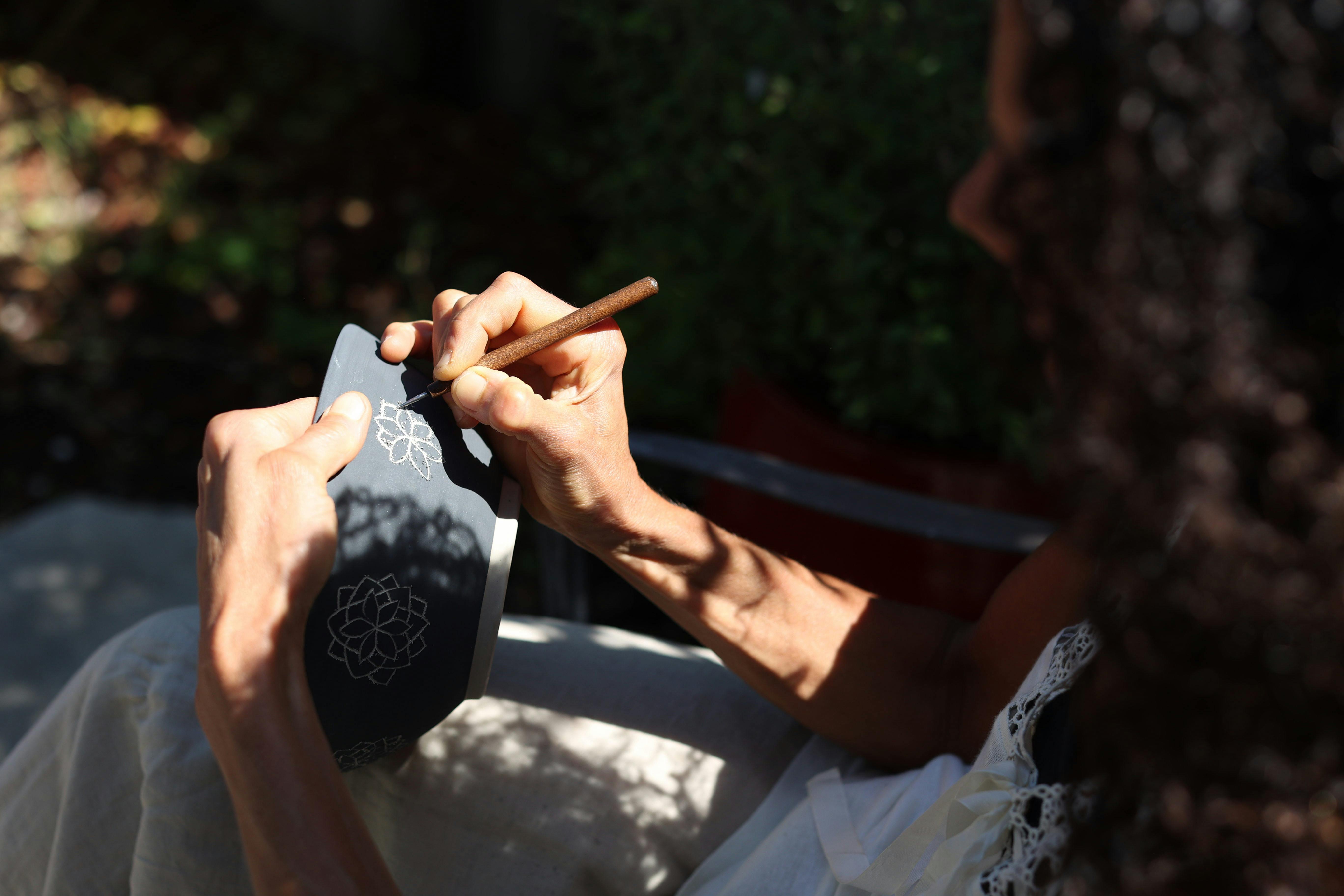 ceramic artist engraving a floral design on a bowl lit by dappled sunlight