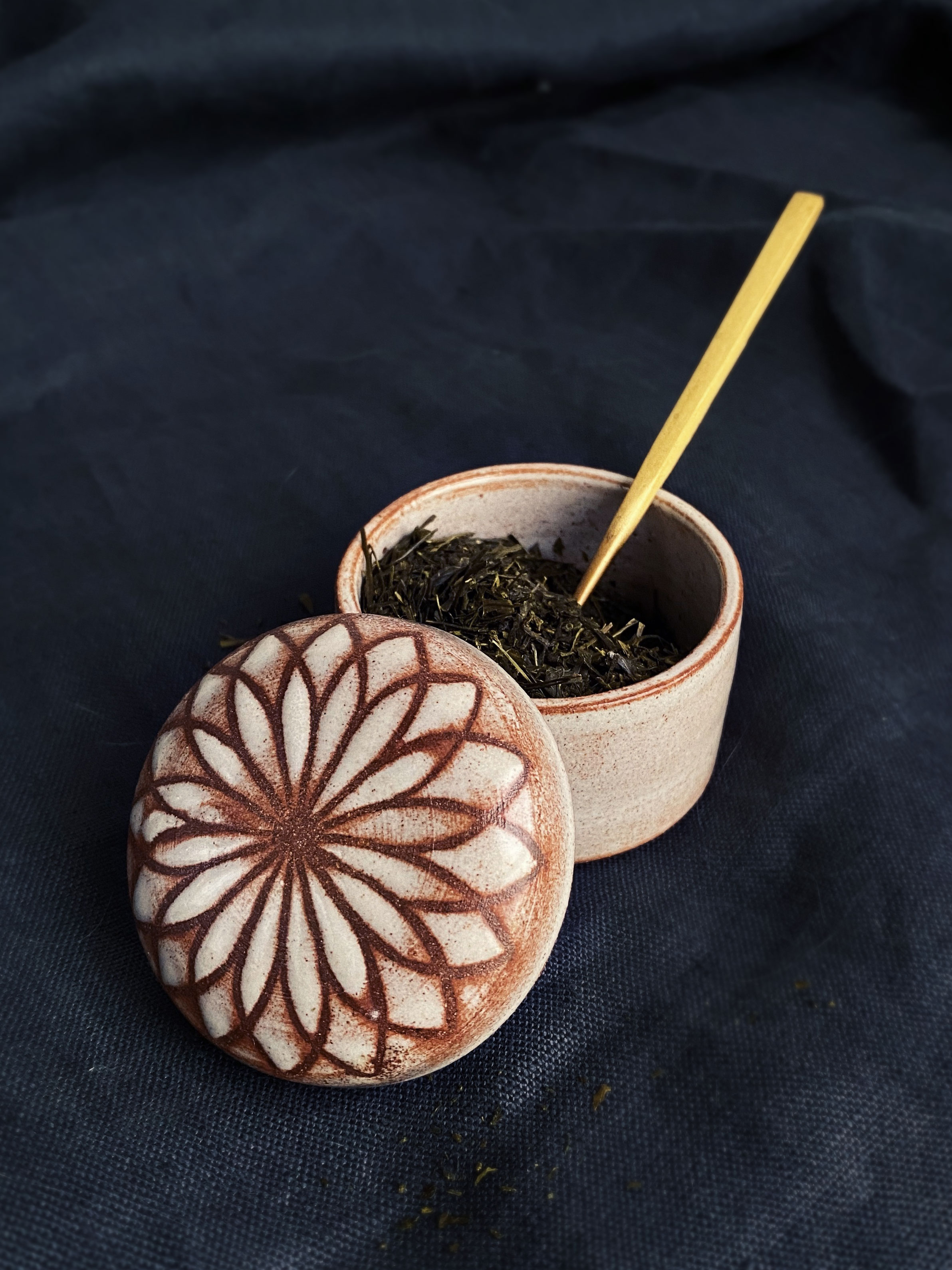 earthtone ceramic jar holding tea leaves and spoon with lid with lotus pattern