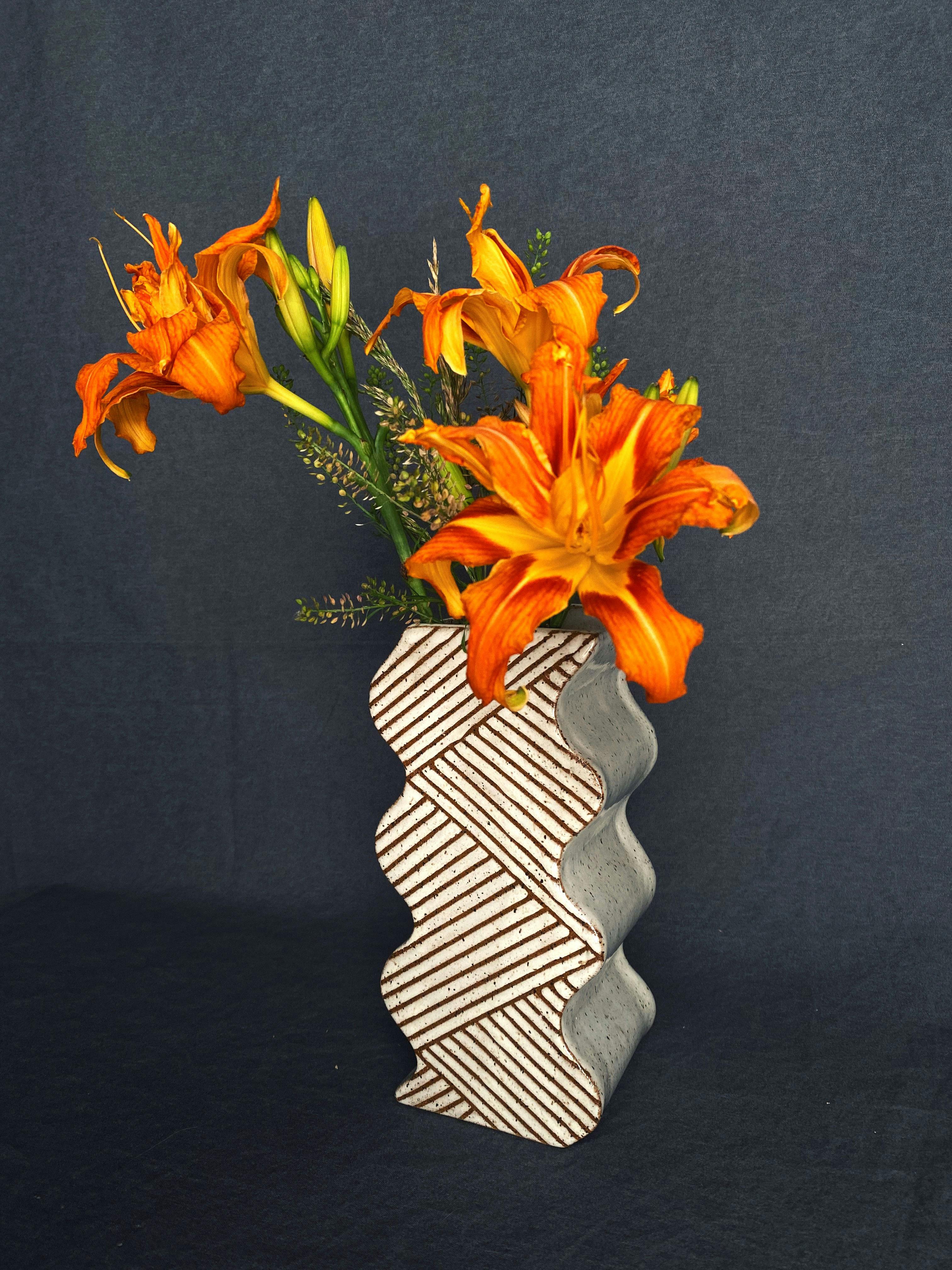 bright orange flowers displayed in earthtone vase with wavey shape weave-like pattern