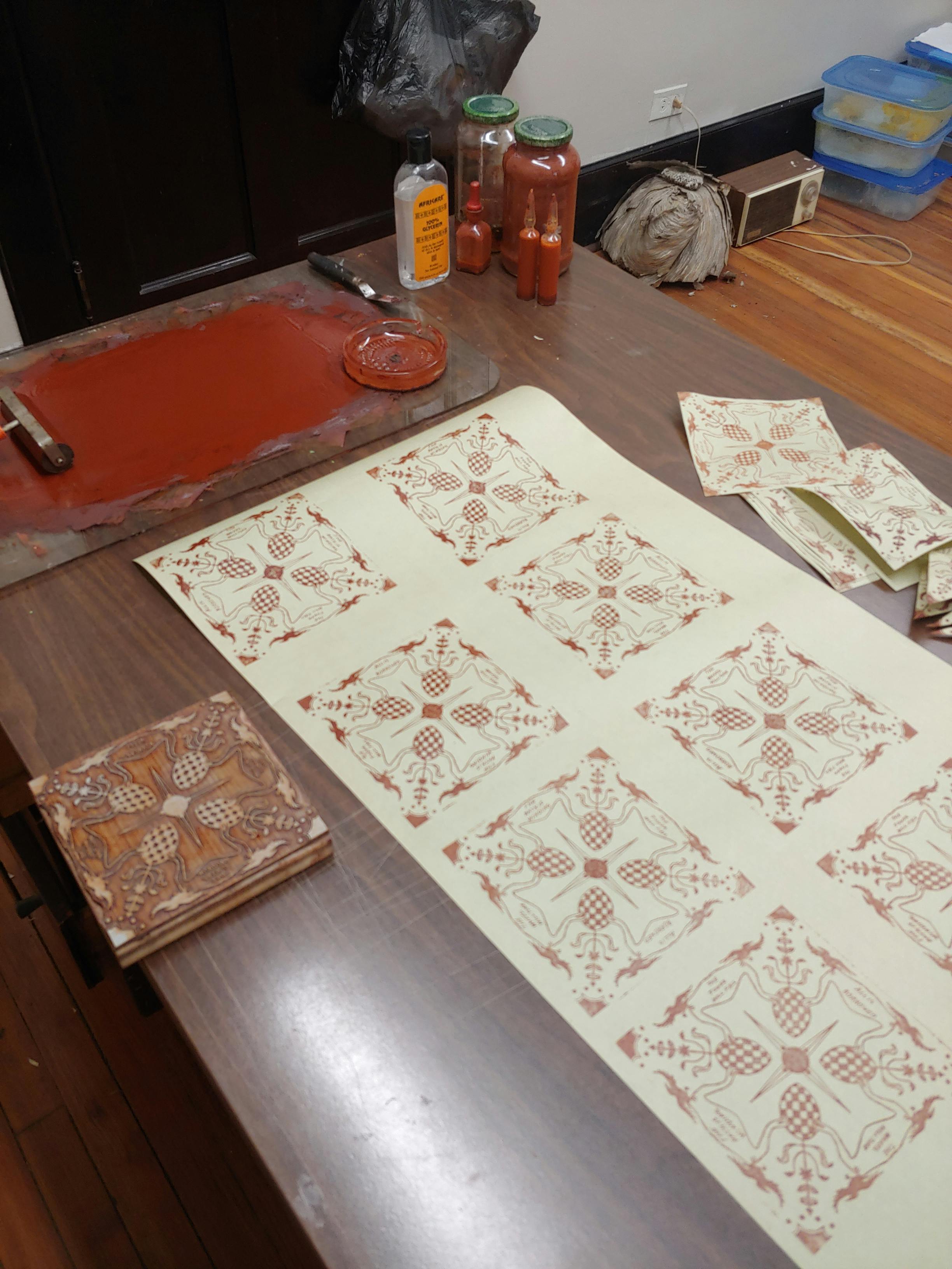 table in studio with printmaking in progress using rust colored ink