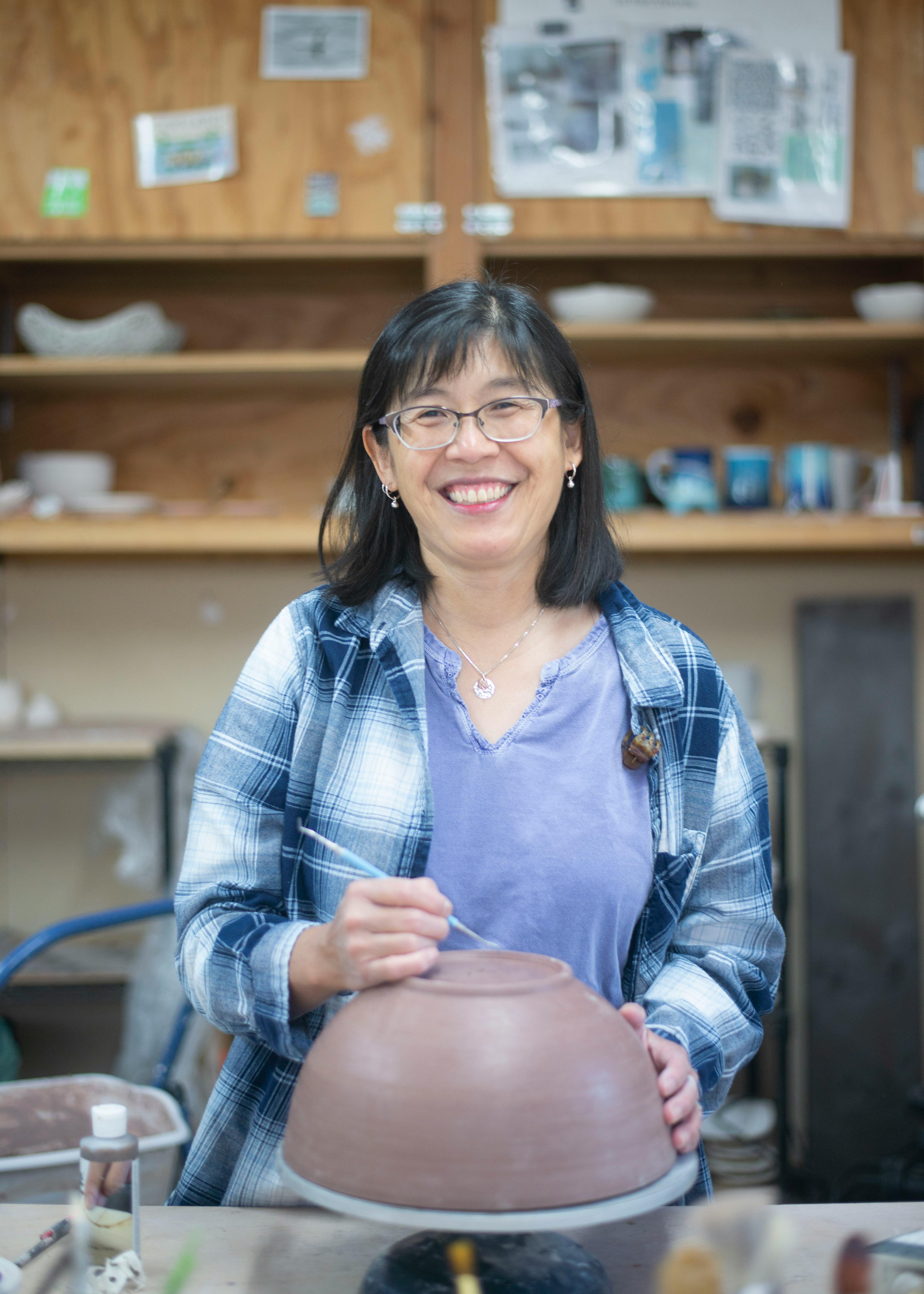 ceramic artist standing in studio smiling and preparing to etch into the bottom of an unfired clay bowl