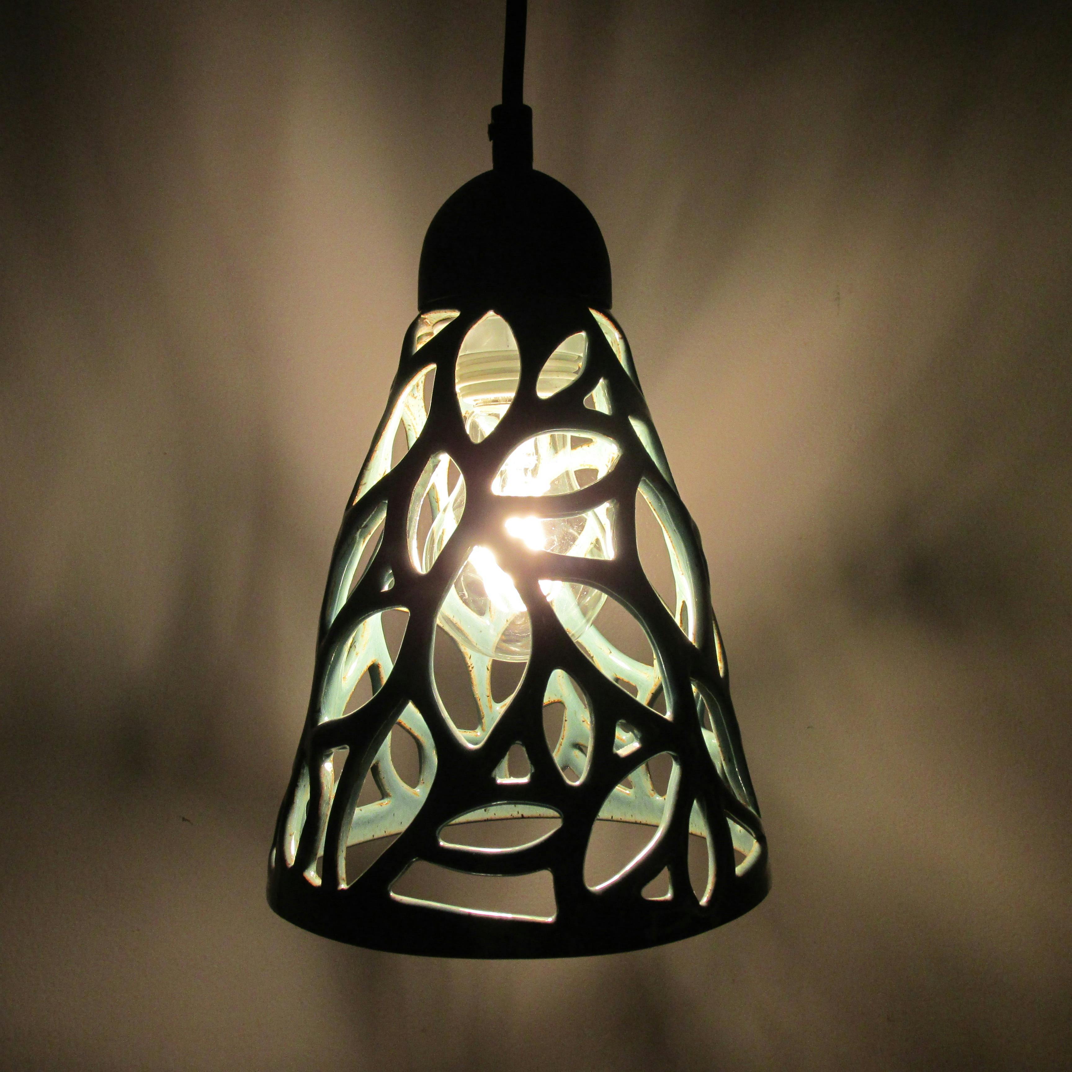 ceramic light fixture with light turned on casting shadows through leaf like patterns into a dark room