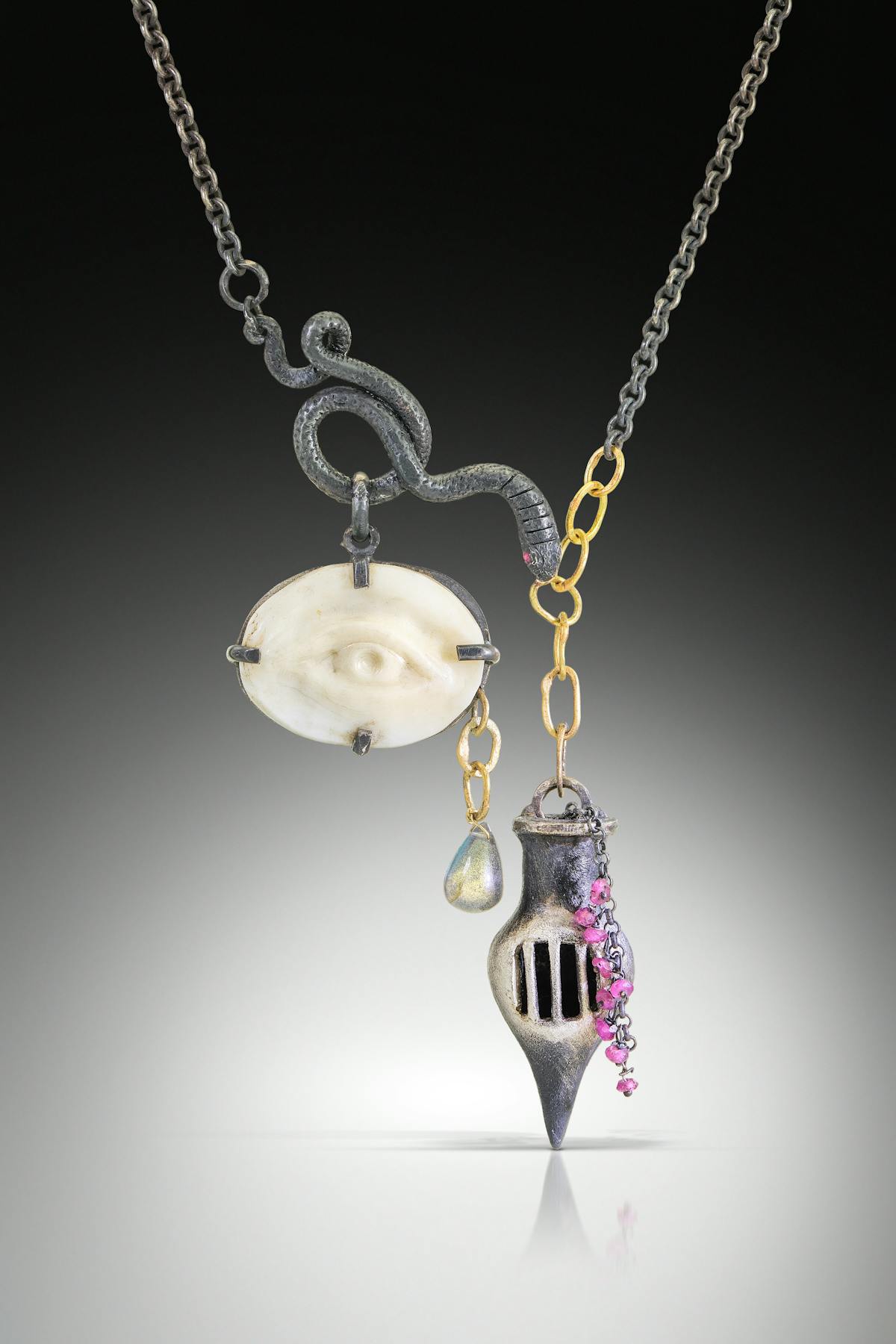 art jewelry necklace feauturing chain with various pendants including eye engraved in shell coiled snack tear drop and small vessel with prison bars
