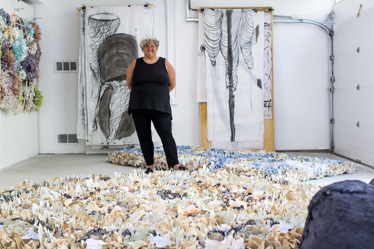artist in studio standing among tapestries made from what appear to be large shells