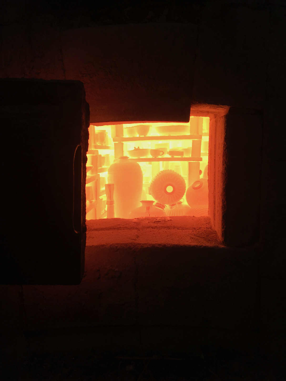 window providing view into a kiln with glowing red ceramics being fired