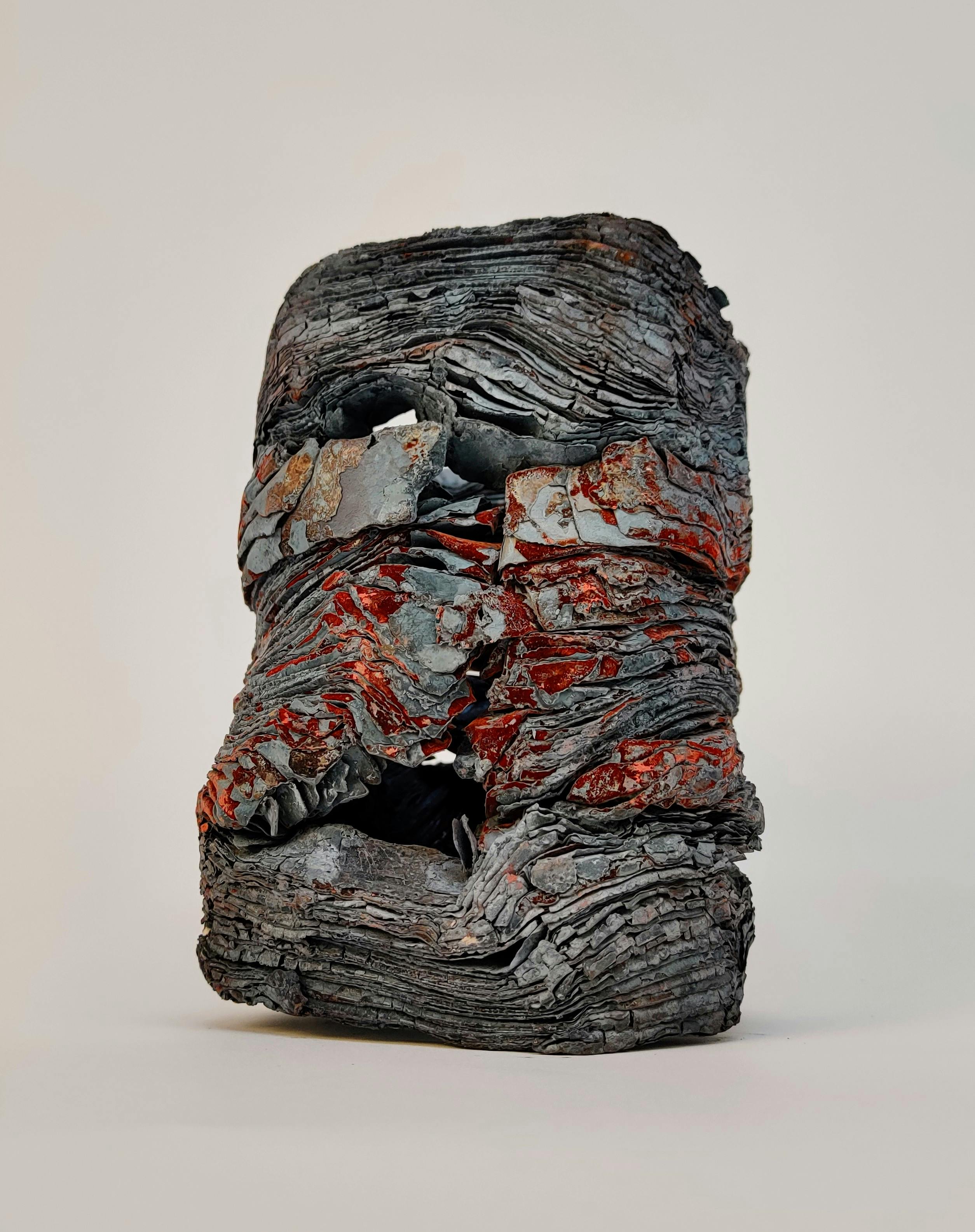 ash colored metal sculpture featuring fine folds and crags with rust accent color reminiscent of leftover coal of a burned log