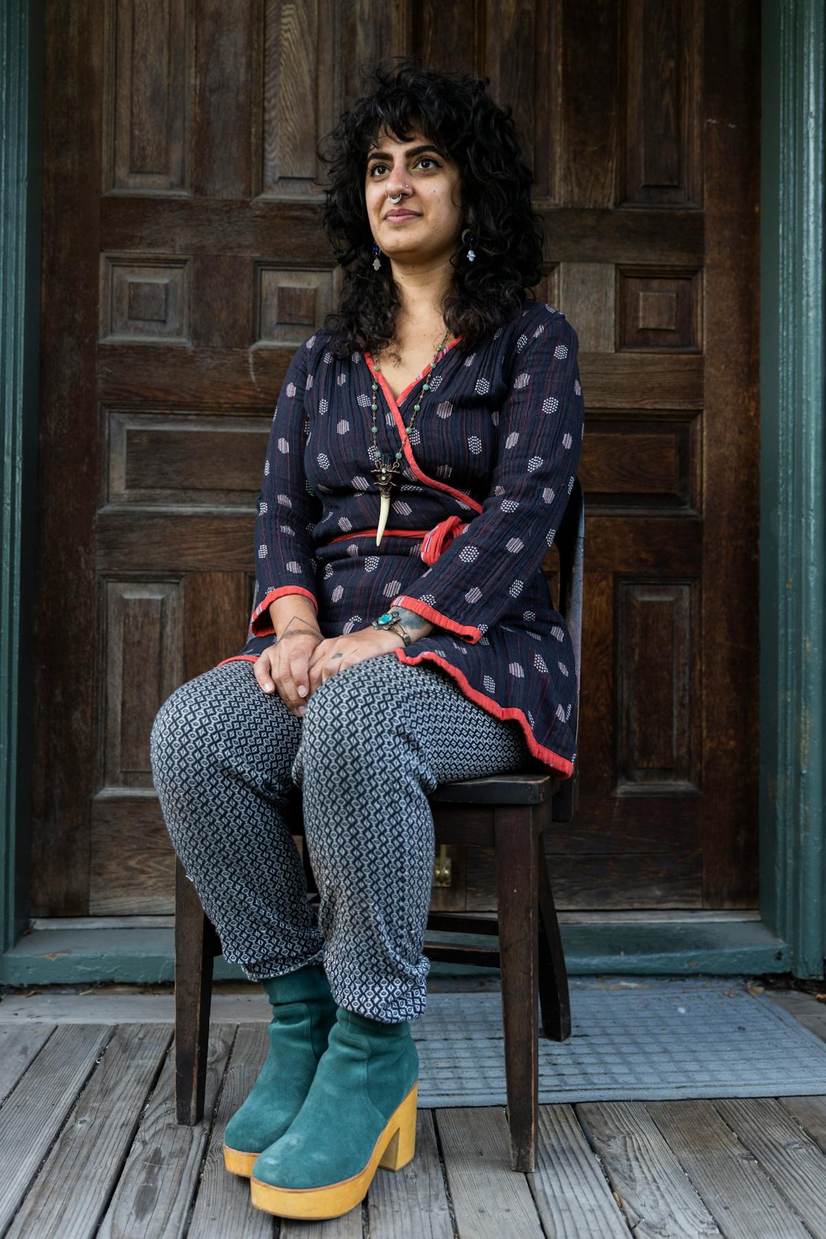 portrait of artist enyo farabi seated on a chair in front of a wooden door