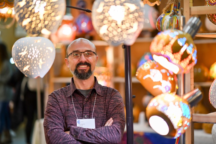 artist standing with arms folded in front of handmade lampshades