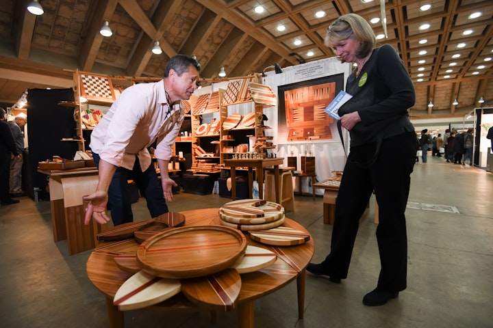artist showing wooden trays to a shopper at a craft fair