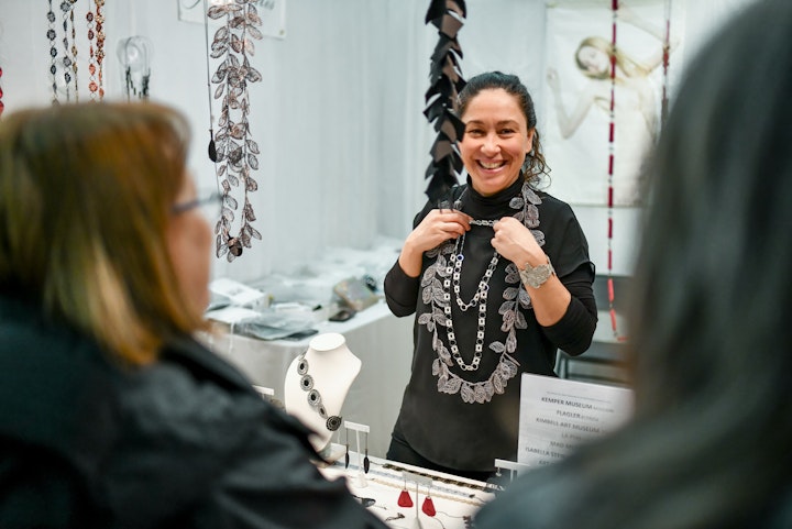Artist showing shoppers jewelry peices at display in craft show