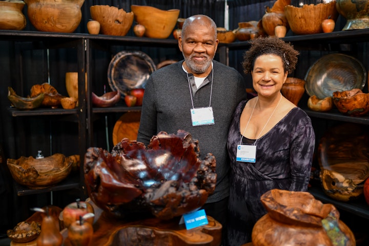 Couple of artists posing amid their assorted handmade bowls in their craft show booth