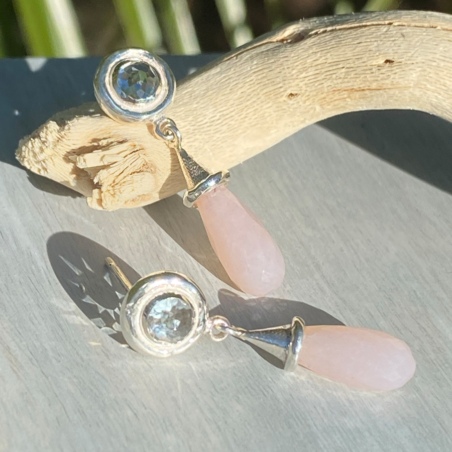 silver pendant earrings with pink stones arranged on piece of driftwood