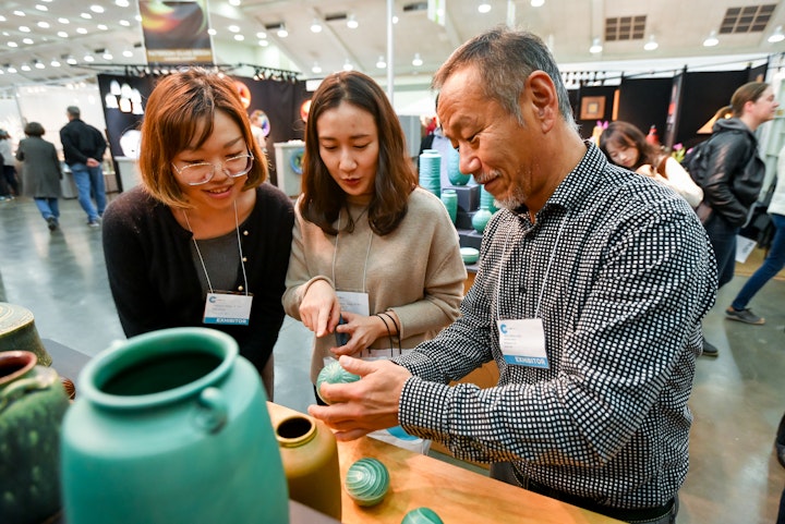 Artist showing students teal ceramic peices at display in craft show